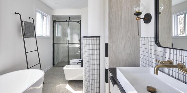 Une salle de bains moderne avec une baignoire blanche autoportante, un porte-serviettes mural, un lavabo rectangulaire avec un robinet en laiton et une douche vitrée. La décoration comprend des carreaux à motifs quadrillés et un grand miroir mural. La lumière naturelle remplit l'espace.